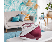 Charger l&#39;image dans la galerie, Un fer à repasser à vapeur sur une planche à repasser, avec un canapé et une décoration en arrière-plan.
