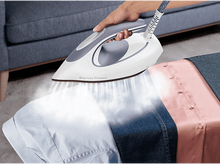 Charger l&#39;image dans la galerie, Une personne repassant des chemises avec un fer blanc et gris, de la vapeur s&#39;élève, chemises à droite.
