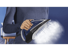 Charger l&#39;image dans la galerie, Une personne repassant avec un fer bleu, dégageant de la vapeur. Un fond bleu et un canapé.
