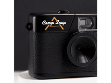Charger l&#39;image dans la galerie, Gros plan sur un appareil photo noir avec les mots &#39;Camp Snap&#39;. L&#39;appareil photo a une prise texturée et un objectif. Le fond est sombre.

