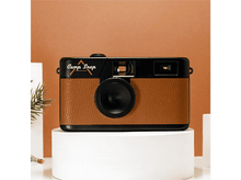 Charger l&#39;image dans la galerie, Un appareil photo marron et noir, étiqueté &quot;Camp Snap&quot;, est posé sur une plateforme blanche, sur fond marron.
