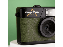 Charger l&#39;image dans la galerie, Appareil photo noir avec cuir vert. Logo &#39;Camp Snap&#39;. Objectif, flash et détails visibles. Le fond est vert.
