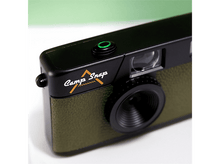 Charger l&#39;image dans la galerie, Gros plan d&#39;un appareil photo noir et vert olive avec les mots &#39;Camp Snap&#39;. L&#39;appareil photo a un objectif et un bouton vert.
