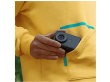 Charger l&#39;image dans la galerie, Personne tenant un appareil photo noir dans la poche d&#39;un sweat à capuche jaune, montrant l&#39;objectif.
