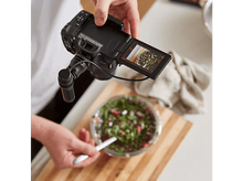 Charger l&#39;image dans la galerie, Une personne tient une caméra filmant une salade dans un bol transparent sur une planche de bois, avec une cuillère.
