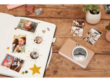 Charger l&#39;image dans la galerie, Un album avec des photos et des autocollants, avec un appareil photo Canon rose sur une table en bois.
