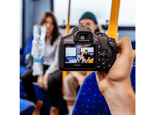 Charger l&#39;image dans la galerie, Une personne tenant un appareil photo Canon, affichant un écran avec deux personnes dans un bus.
