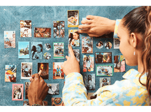 Charger l&#39;image dans la galerie, Des personnes organisant des photos sur un mur bleu, avec de nombreuses images dans des cadres de tailles variées.
