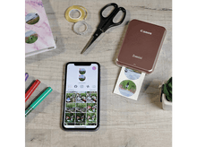 Charger l&#39;image dans la galerie, Imprimante mobile imprimant une photo, téléphone affichant des photos, ciseaux, ruban adhésif et stylos sur bois.
