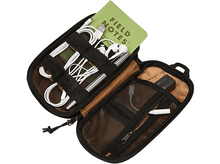 Charger l&#39;image dans la galerie, Étui organisateur noir zippé ouvert, avec divers articles tels que des câbles, un stylo et un bloc-notes à l&#39;intérieur.
