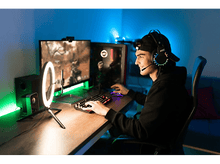 Charger l&#39;image dans la galerie, Joueur portant un casque, jouant à un bureau avec un moniteur et une lampe annulaire. Lumières bleues et violettes.
