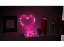 Charger l&#39;image dans la galerie, Une lumière en forme de cœur au néon sur un mur, avec une étagère en dessous contenant des livres et une petite plante.
