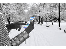 Charger l&#39;image dans la galerie, Personne gantée utilisant un téléphone dans un parc enneigé avec bancs et arbres.
