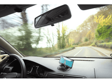 Charger l&#39;image dans la galerie, Un téléphone dans un support de voiture sur le tableau de bord. La route et un rétroviseur sont visibles en arrière-plan.
