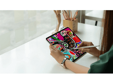 Charger l&#39;image dans la galerie, Une personne utilisant une tablette avec un stylet, affichant une œuvre d&#39;art abstraite colorée sur une table blanche.
