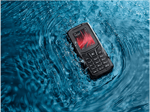 Charger l&#39;image dans la galerie, Un téléphone noir robuste flotte dans l&#39;eau bleue. L&#39;écran affiche l&#39;heure et un design rouge.
