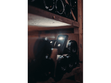 Charger l&#39;image dans la galerie, Un appareil noir est placé dans une cave à vin, entouré de bouteilles de vin.
