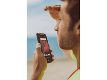 Charger l'image dans la galerie, Homme regardant l'écran de son téléphone sur la plage. Plage et eau en arrière-plan.
