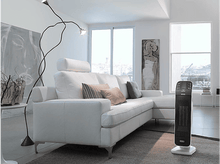 Charger l'image dans la galerie, Salon avec canapé blanc, tapis gris, lampadaire et un radiateur DeLonghi noir sur pied.
