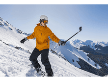 Charger l&#39;image dans la galerie, Un snowboarder prenant un selfie sur une montagne enneigée sous un ciel clair.
