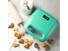 Charger l'image dans la galerie, Un gaufrier vert avec des biscuits, un rouleau à pâtisserie et un pot à sucre sur une table.
