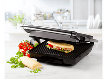 Charger l&#39;image dans la galerie, Une presse à panini avec un sandwich, des tomates, du basilic et d&#39;autres ingrédients sur une surface blanche.
