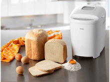 Charger l&#39;image dans la galerie, Une machine à pain avec deux pains, des tranches, des œufs et de la farine sur un comptoir de cuisine.
