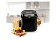 Charger l&#39;image dans la galerie, Machine à pain noire avec pain et confiture sur une planche en bois et tranches de pain. Fond blanc.
