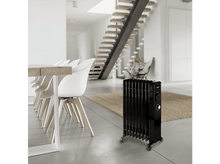 Charger l&#39;image dans la galerie, Un radiateur à huile noir sur roulettes dans une pièce. Une table et des chaises blanches en arrière-plan.
