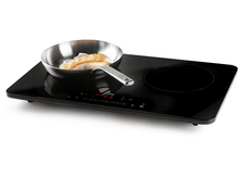 Charger l&#39;image dans la galerie, Plaque à induction noire avec une poêle de saumon. La plaque est allumée et possède un panneau de commande.

