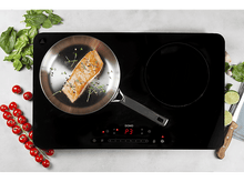 Charger l&#39;image dans la galerie, Plaque à induction noire avec poêle et nourriture. Ingrédients autour.
