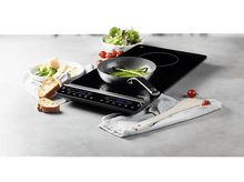 Charger l&#39;image dans la galerie, Plaque à induction noire avec nourriture dessus. Comprend une poêle, des asperges et du pain. Cuillère en bois.
