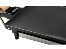 Charger l&#39;image dans la galerie, Gros plan d&#39;une plaque chauffante noire avec une poignée en bois, inclinée sur un fond blanc.
