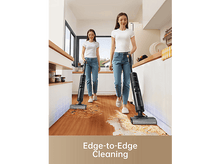 Charger l&#39;image dans la galerie, Deux femmes nettoient le sol d&#39;une cuisine avec des aspirateurs noirs. Texte en bas : Nettoyage bord à bord.
