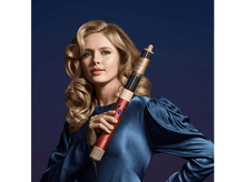 Charger l&#39;image dans la galerie, Femme blonde bouclée avec un styler à cheveux. Elle porte une robe bleue, sur un fond bleu dégradé.
