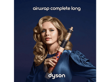 Charger l&#39;image dans la galerie, Une femme tenant un styler capillaire Dyson Airwrap rose et rouge, sur fond bleu foncé.
