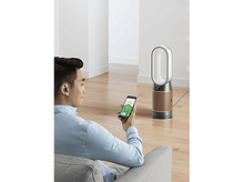 Charger l&#39;image dans la galerie, Un homme utilise un smartphone pour contrôler un ventilateur intelligent blanc et doré dans un salon.
