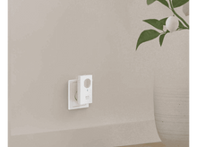 Charger l&#39;image dans la galerie, Une sonnette intelligente blanche branchée sur une prise murale sur un mur beige clair.
