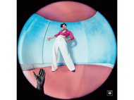 Harry Styles en chemise rose et pantalon blanc, dans une pièce rose et bleue, avec une main.