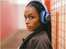 Charger l&#39;image dans la galerie, Une femme aux tresses portant un casque bleu regarde la caméra. Fond rouge et blanc.
