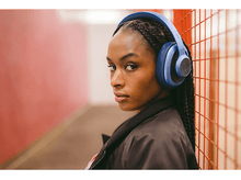 Charger l&#39;image dans la galerie, Une femme noire porte un casque bleu devant un mur rouge. Regarde la caméra.
