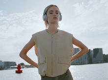 Charger l&#39;image dans la galerie, Femme avec un casque et un gilet debout dehors, mains sur les hanches. Ciel et eau.
