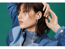 Charger l&#39;image dans la galerie, Une femme portant des écouteurs blancs et une veste en jean, regardant vers la gauche. Fond vert.
