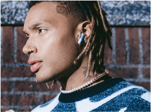Charger l&#39;image dans la galerie, Homme avec des écouteurs bleus et blancs dans l&#39;oreille. Il porte un collier de perles et a un tatouage.
