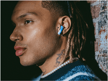 Charger l'image dans la galerie, Homme avec des écouteurs bleus et blancs dans l'oreille. Il porte un collier de perles et a un tatouage.
