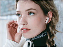 Charger l'image dans la galerie, Femme avec écouteur blanc dans l'oreille. Cheveux blonds, yeux bleus. Col roulé vert, haut blanc.
