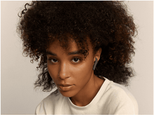 Charger l'image dans la galerie, Une femme aux cheveux bouclés foncés porte une chemise blanche et des écouteurs gris foncés.
