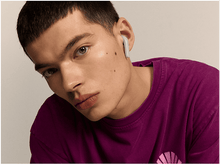 Charger l'image dans la galerie, Un jeune homme avec un écouteur dans l'oreille, regardant la caméra. Fond clair.
