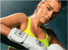 Charger l'image dans la galerie, Femme blonde sur un ring, haut jaune et gants blancs, regardant la caméra.
