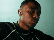 Charger l'image dans la galerie, Un homme portant un écouteur dans une oreille, regardant vers le côté droit du cadre.
